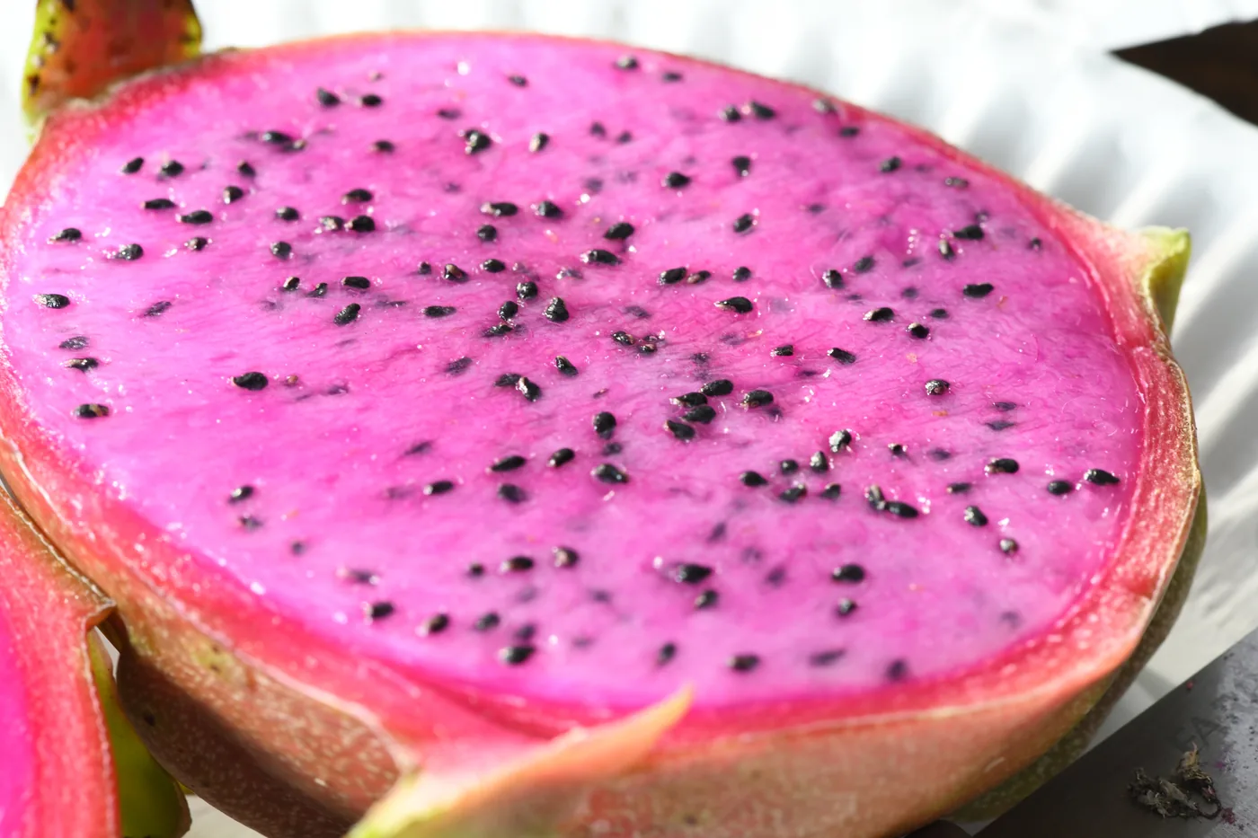 A halved red-fleshed dragon fruit with bright magenta flesh and black seeds