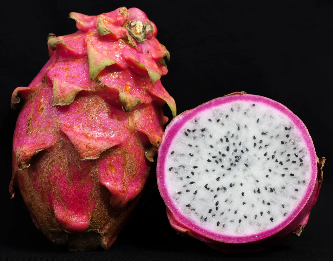 A whole dragon fruit beside a halved fruit showing white flesh