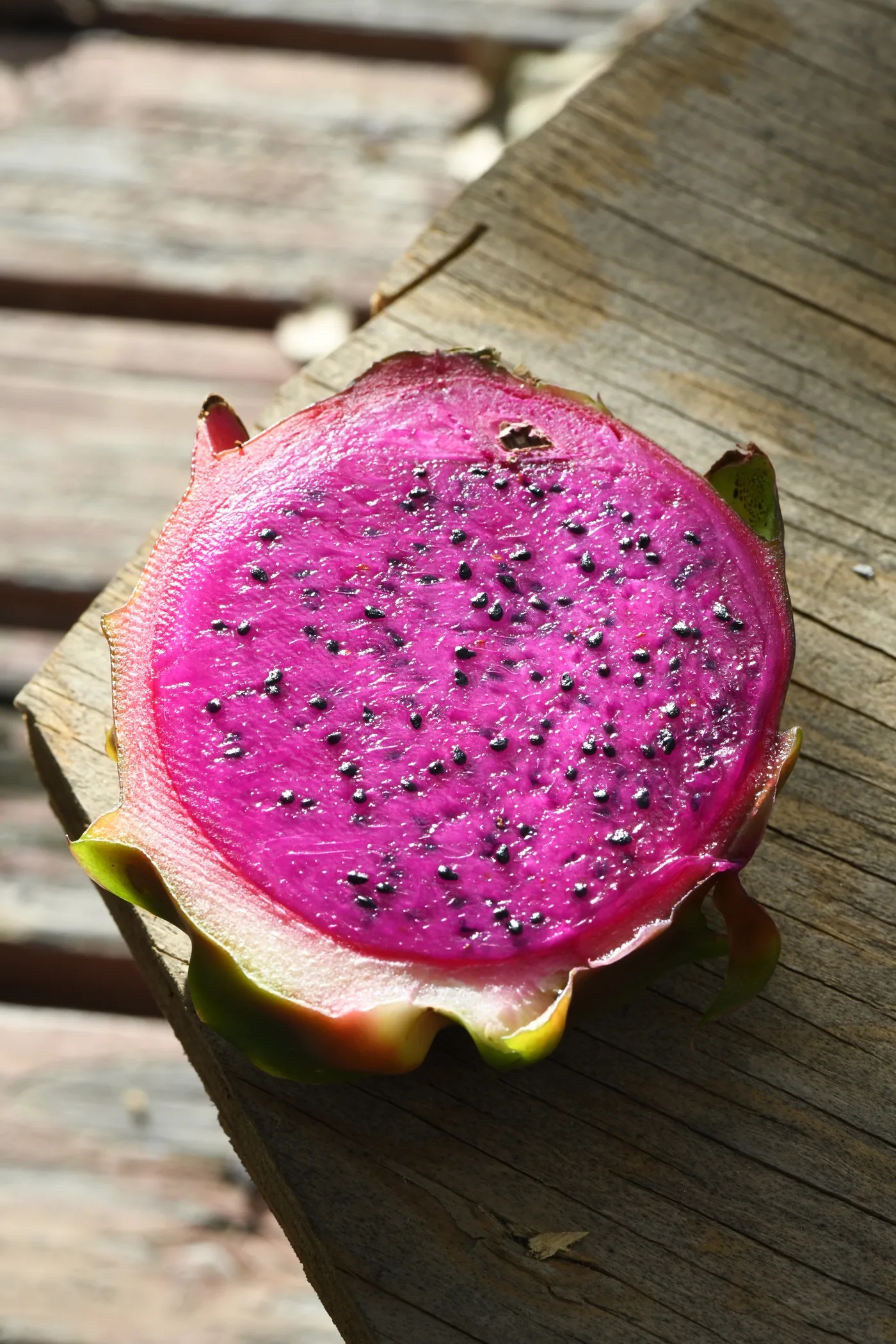 A halved red-fleshed dragon fruit sitting on wood