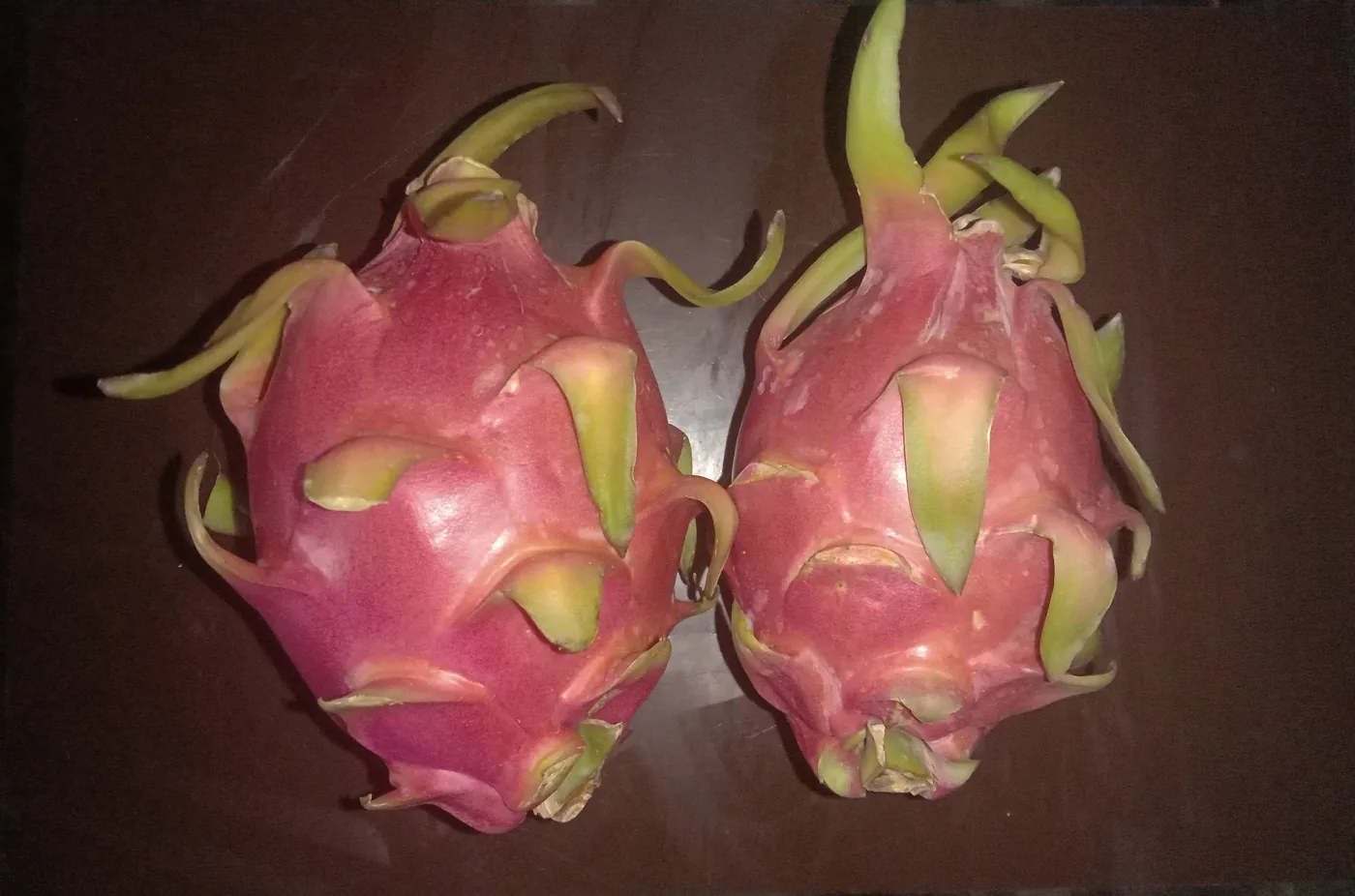 Two whole pink dragon fruit on a dark surface