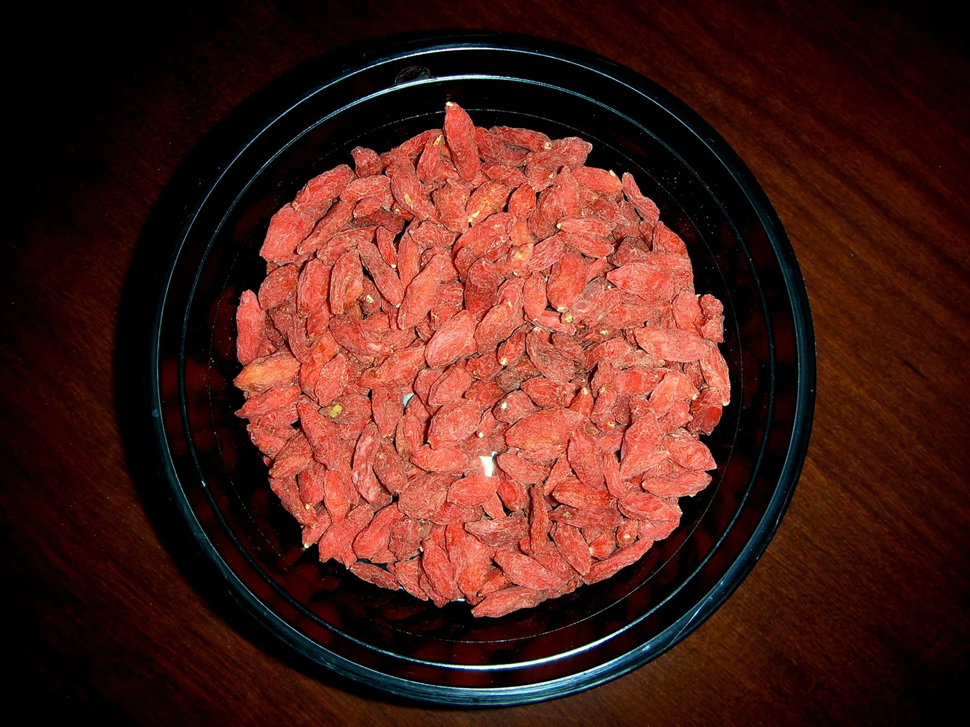 Dried goji berries piled in a black bowl on a wooden table