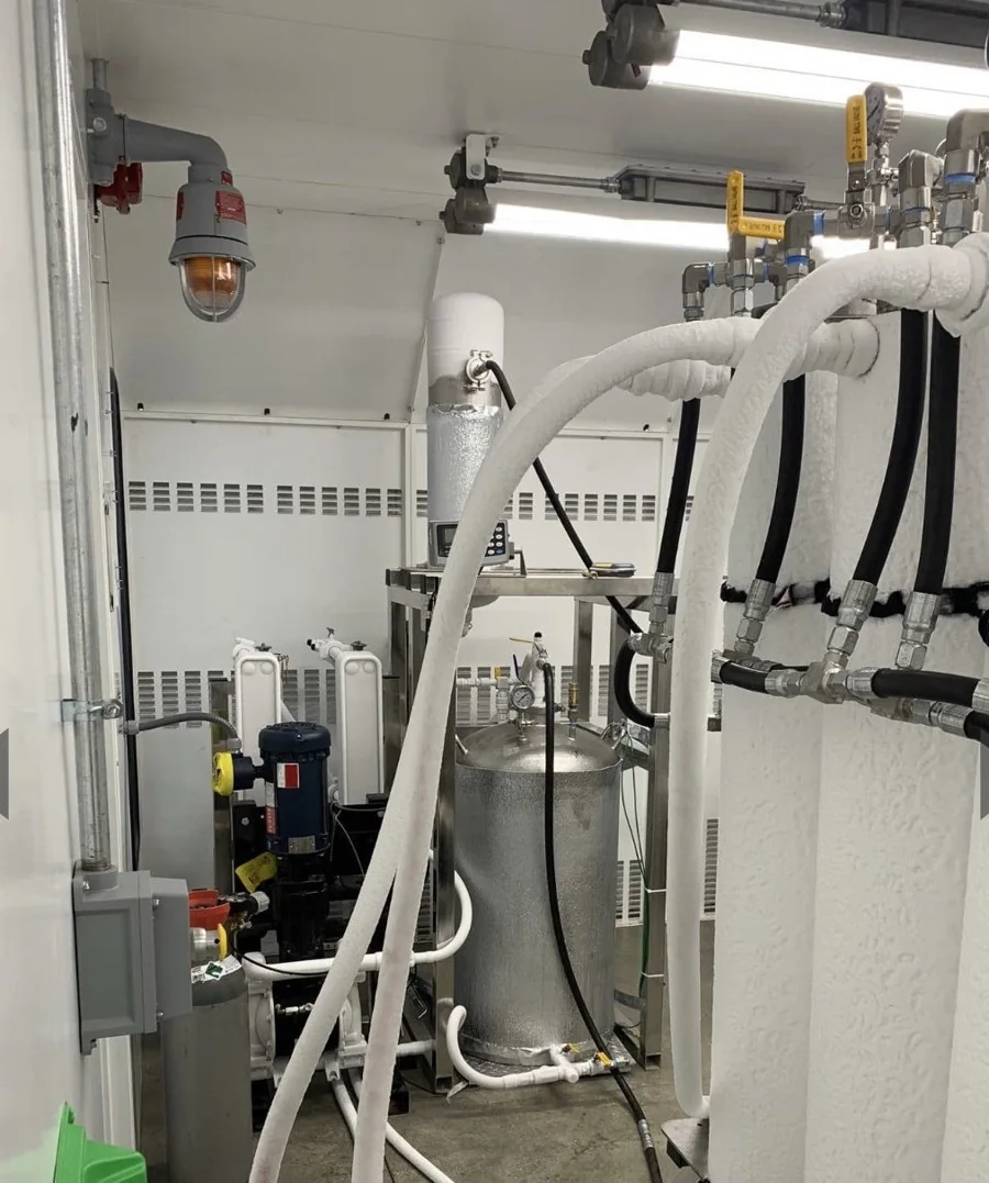 White hoses, vessels and valves along the wall of an extraction room