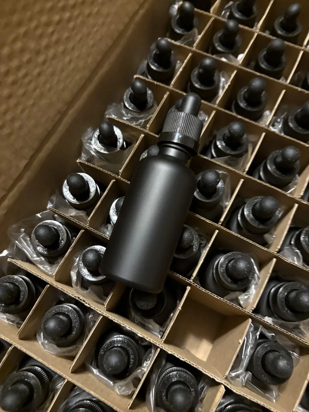 A black glass tincture bottle standing in a grid of bottle caps in a box